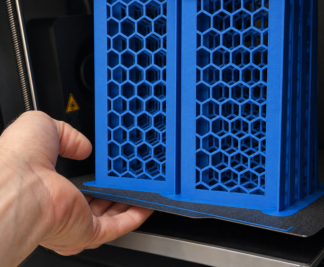 A hand lifting a flexible build plate of blue honeycomb Slabster risers out of a 3D printer