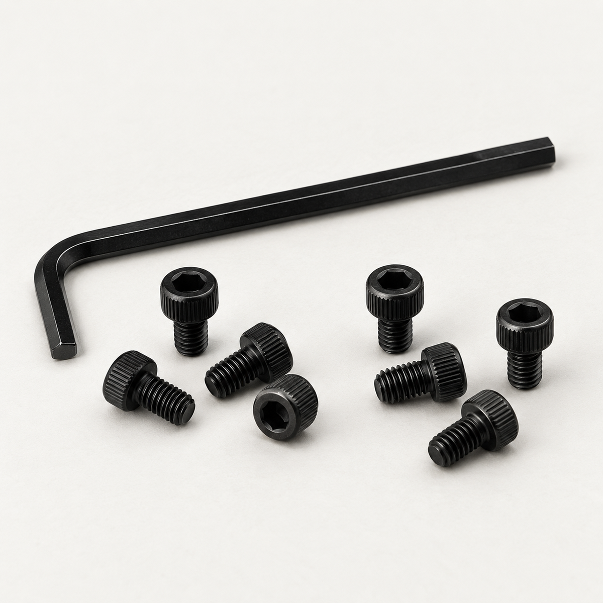 Eight black M3 socket head screws scattered in front of a black 2.5 mm hex key, shown at an angle